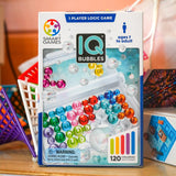 IQ Bubbles game box by Smart Games on a table with colorful marbles.
