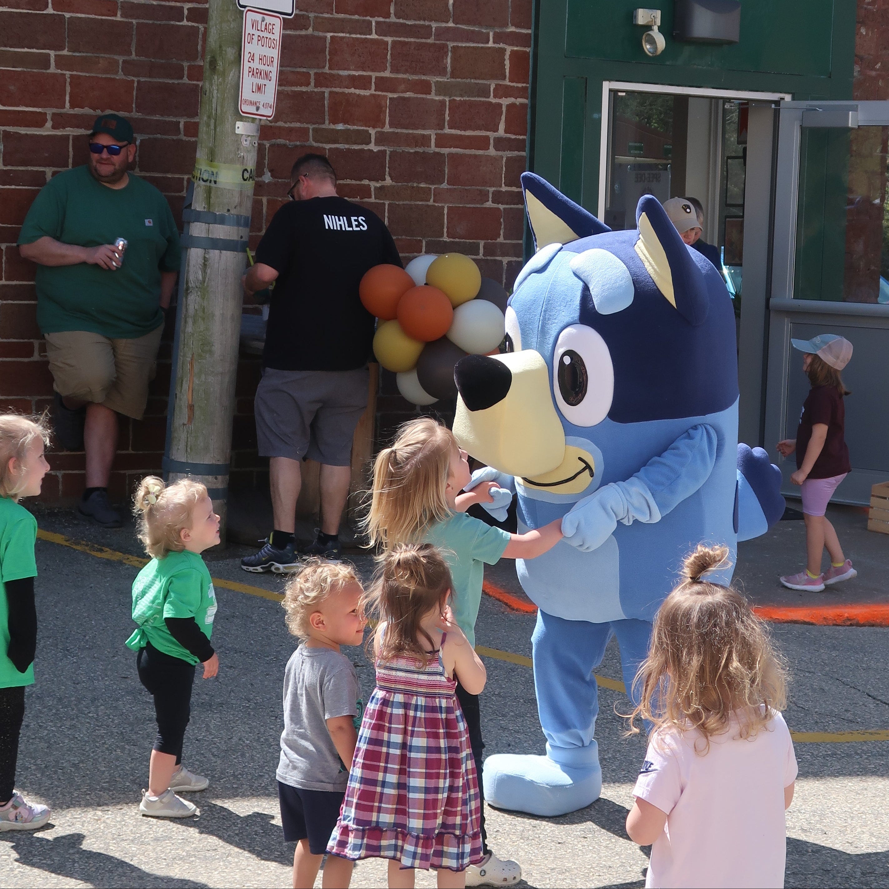 Children interacting with a blue mascot outside a building with 'Pages & Parcels' sign.