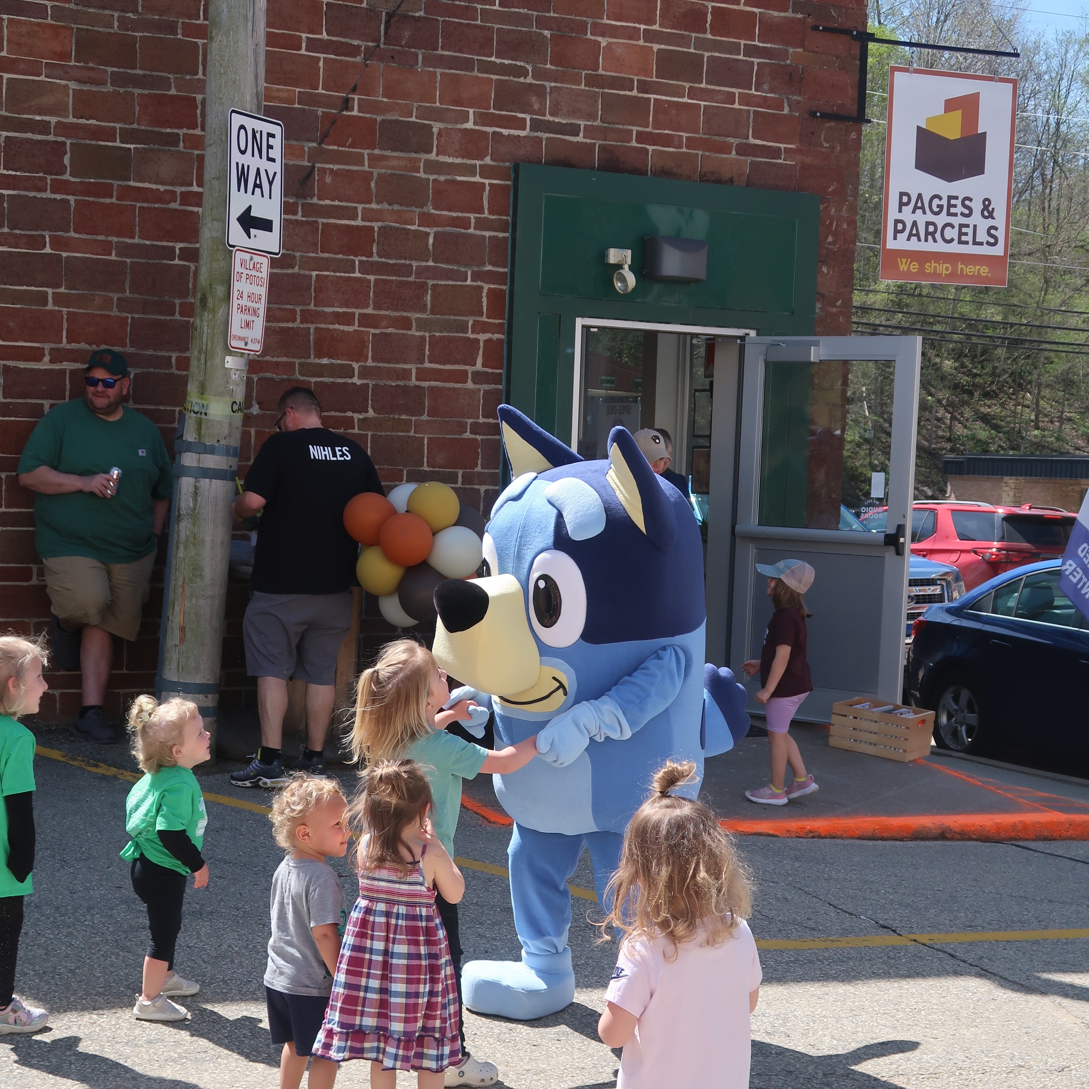 Children interacting with a blue mascot outside a building with 'Pages & Parcels' sign.