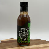 Bottle of Competition Series sauce on a wooden cutting board with a white background