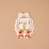 Pair of earrings in a 'The Darling Effect' packaging on a beige background