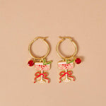 Gold hoop earrings with wine glass and bow designs on a beige background