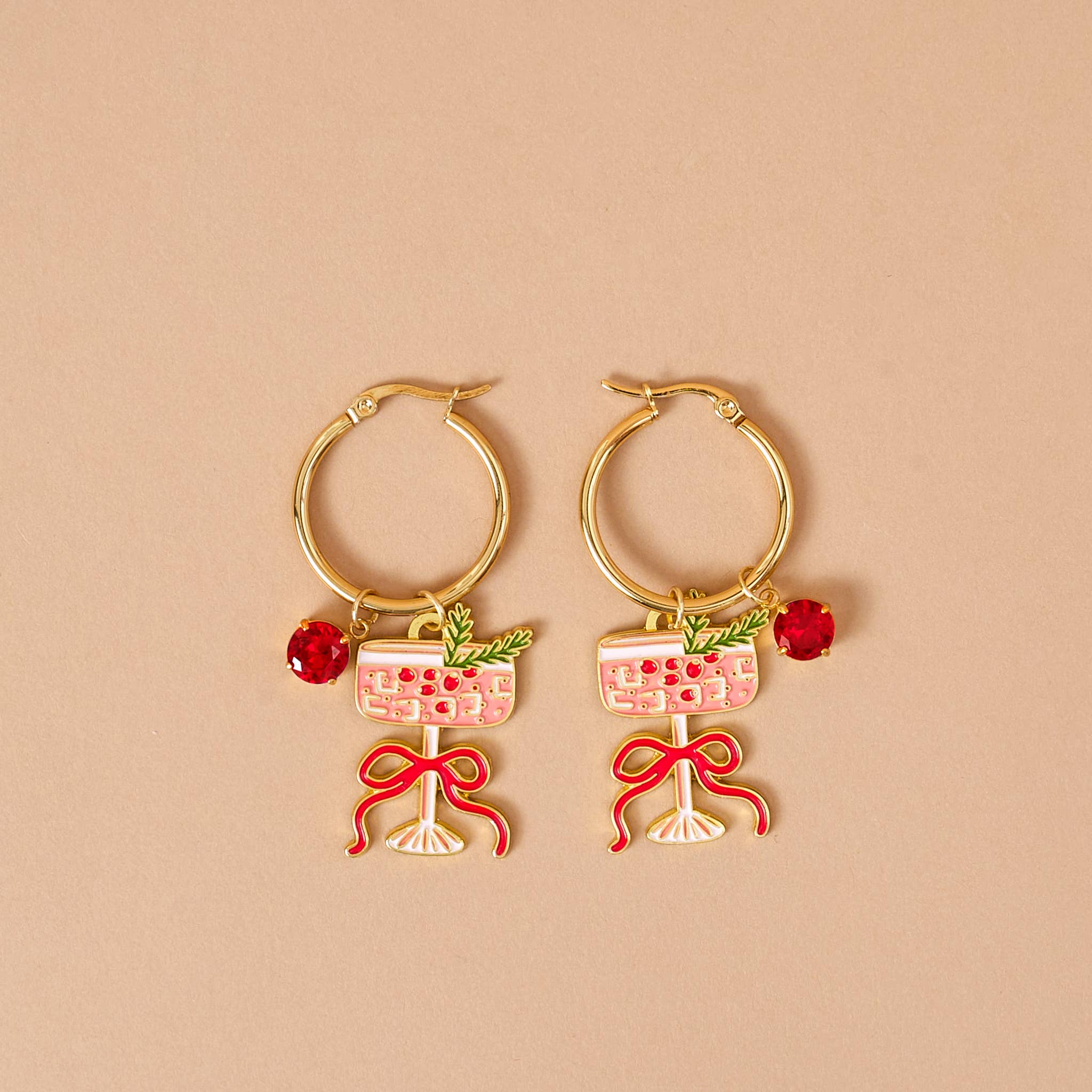 Gold hoop earrings with wine glass and bow designs on a beige background