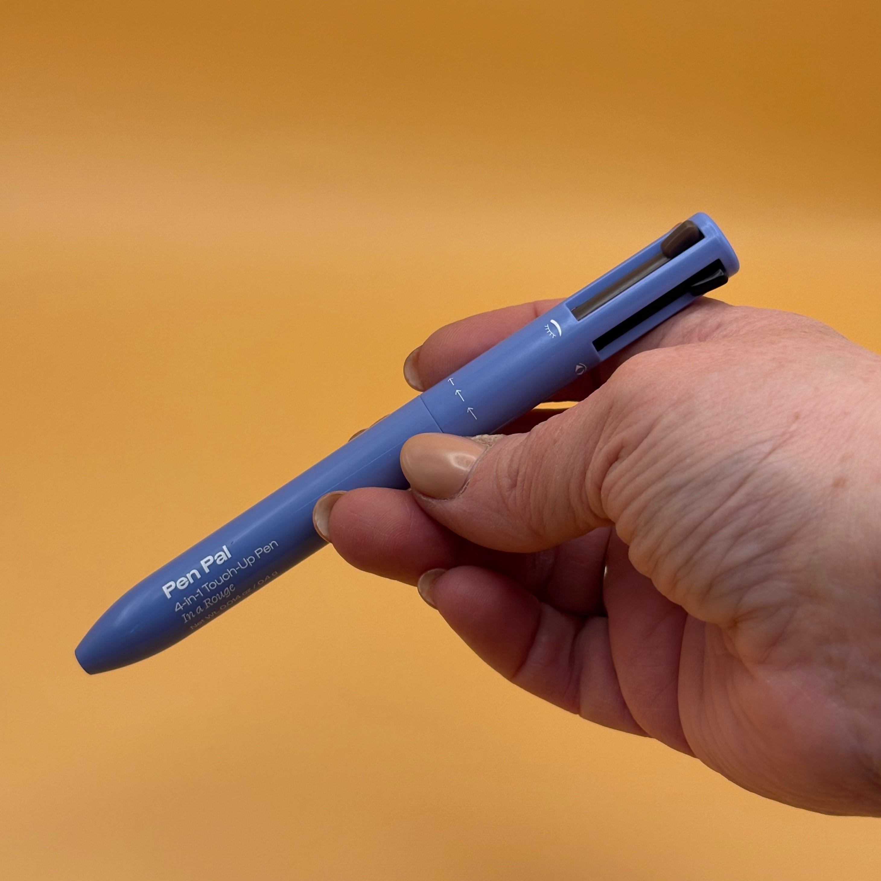 Hand holding a blue alleyoop pen pal in a rouge color with a clear cartridge on an orange background