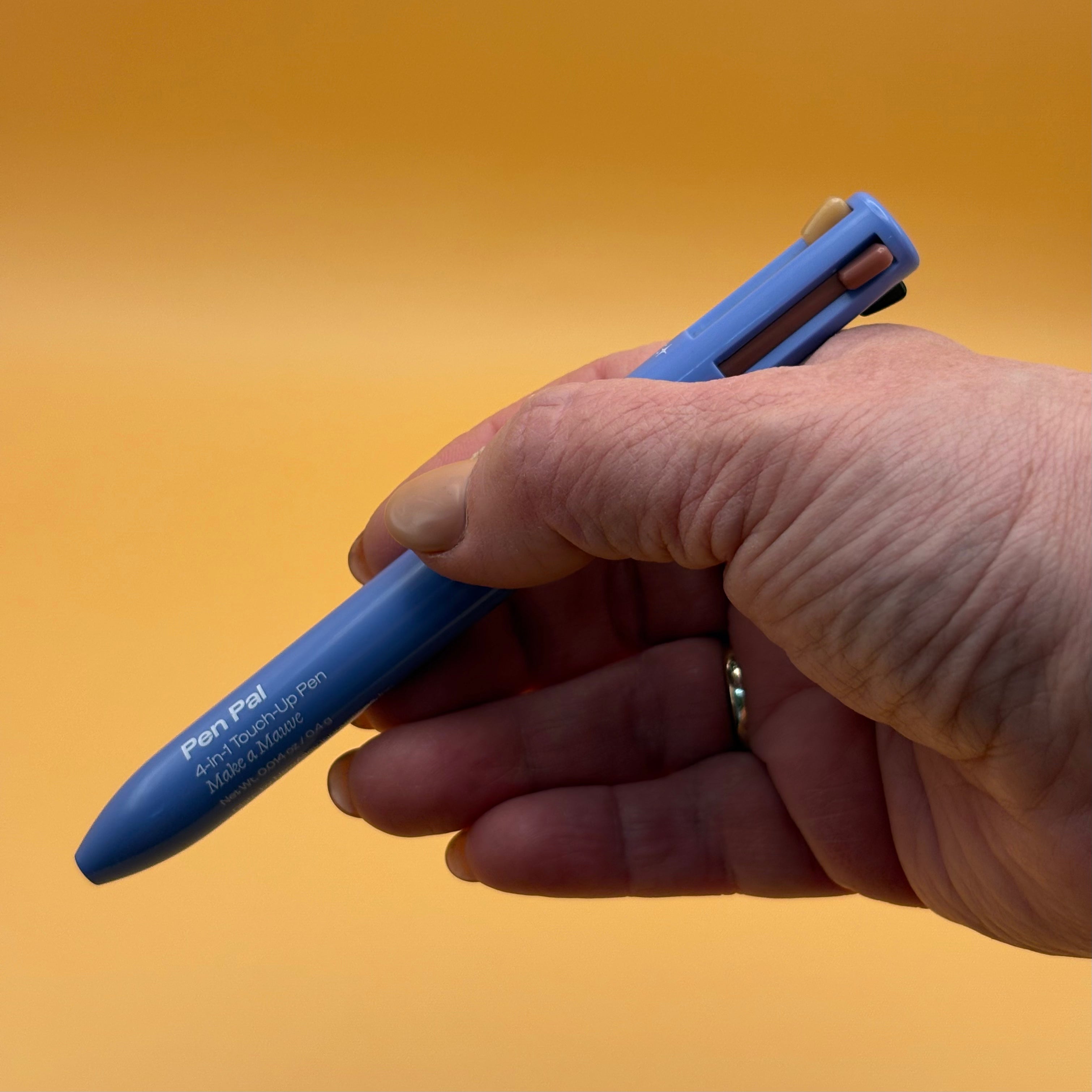 Hand holding a blue alleyoop pen pal make a mauve color against an orange background