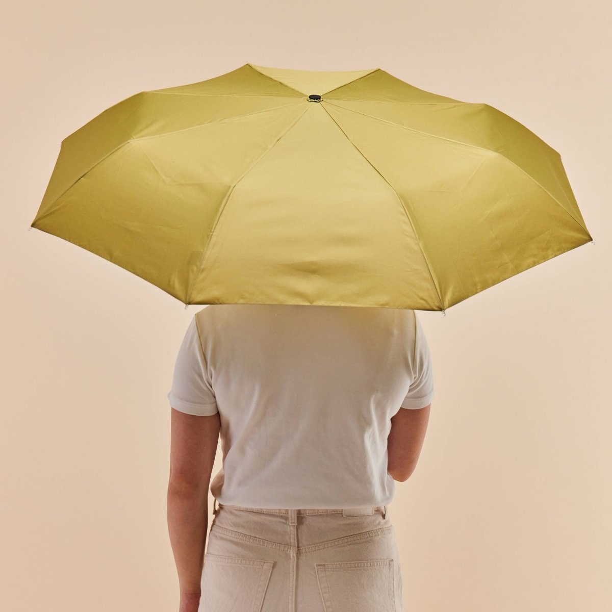 Person holding a yellow duckhead umbrella against a beige background