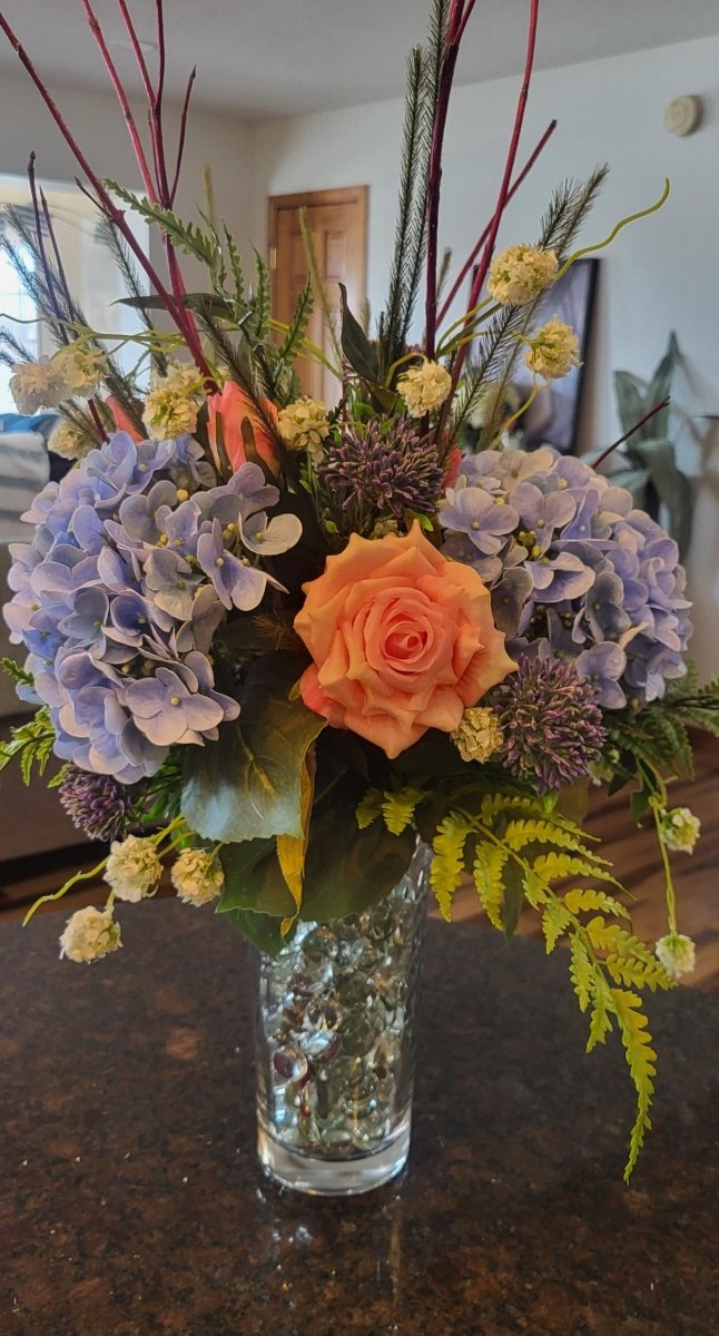 Floral arrangement with a variety of flowers in a clear vase on a dark surface.
