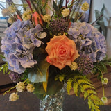 Floral arrangement with a variety of flowers in a clear vase on a dark surface.