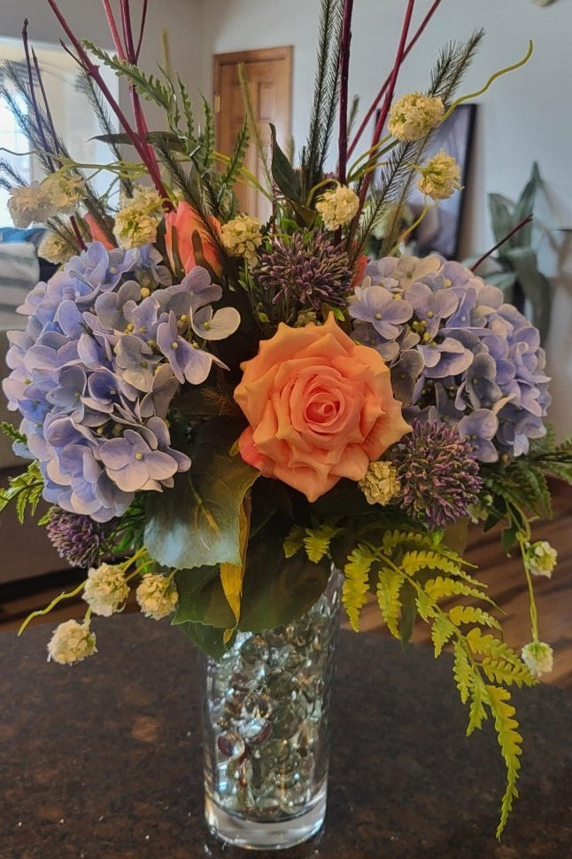 Floral arrangement with a variety of flowers in a clear vase on a dark surface.