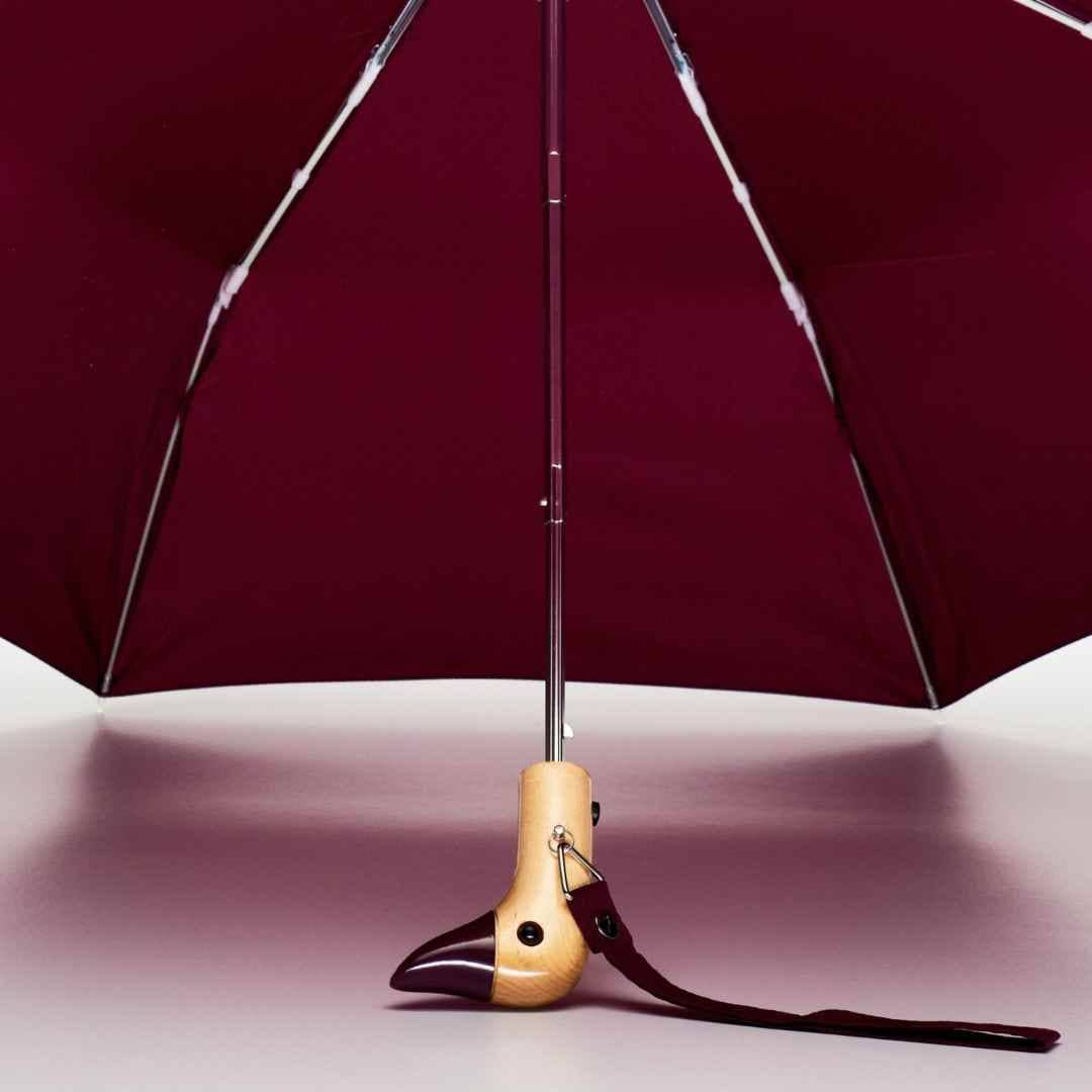 Maroon duckhead umbrella with wooden handle and strap on a light pink background