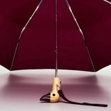 Maroon duckhead umbrella with wooden handle and strap on a light pink background