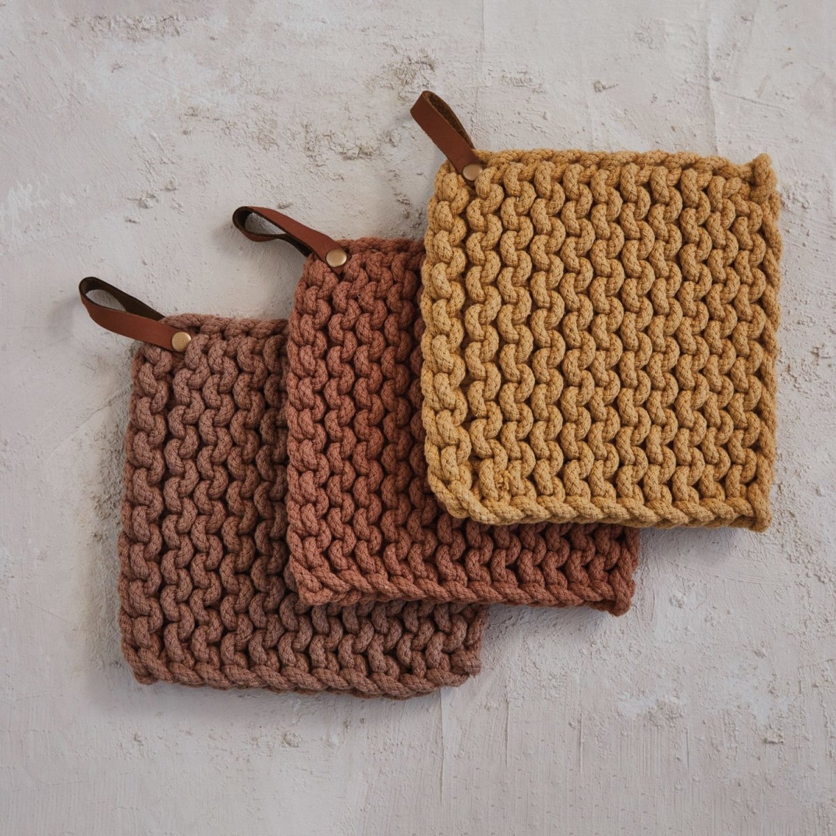 The crocheted pot holder hanging by its leather loop, showing the crochet texture