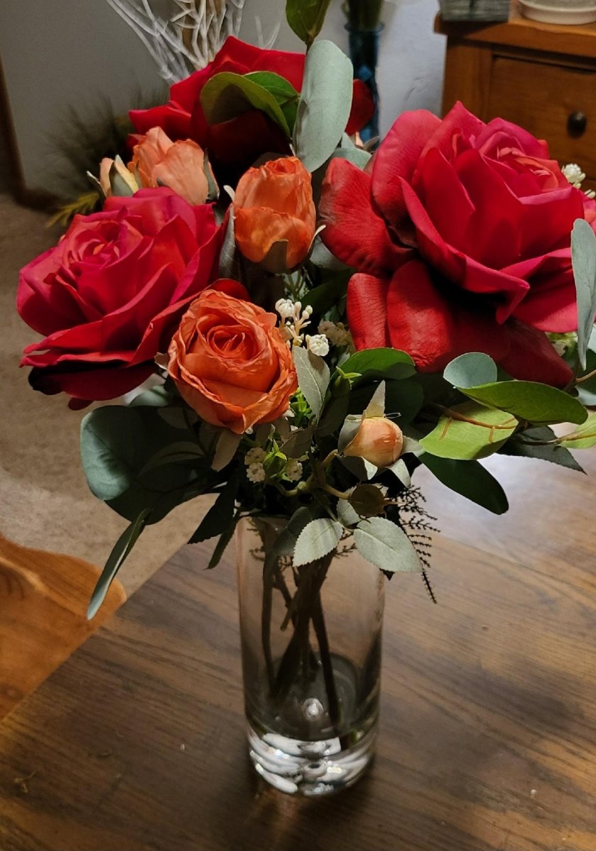 Bouquet of red and orange roses in a clear vase on a wooden table.