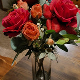 Bouquet of red and orange roses in a clear vase on a wooden table.
