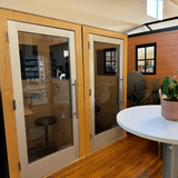 Small sound booths with wooden walls, glass doors, and a white table with a plant.