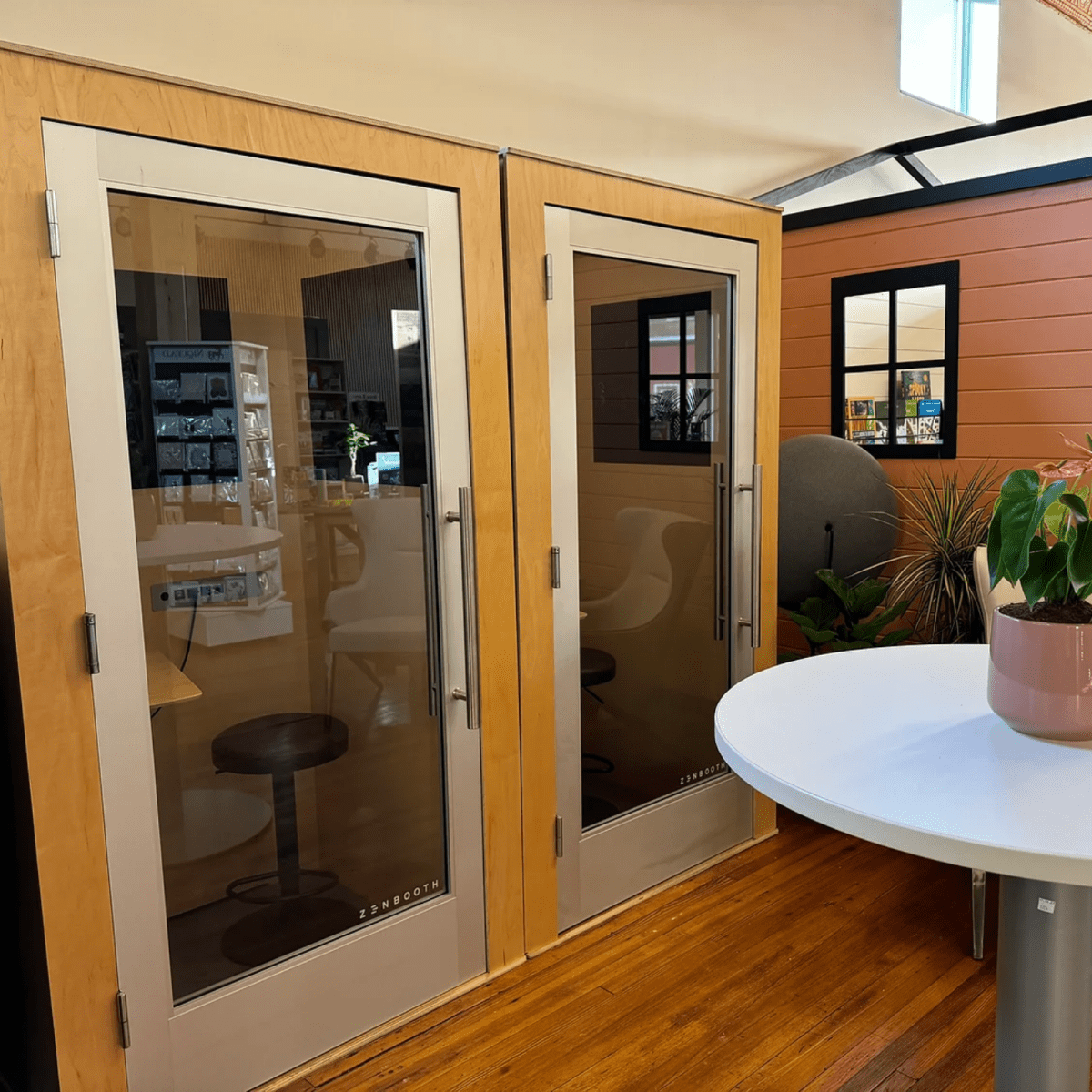 Small sound booths with wooden walls, glass doors, and a white table with a plant.