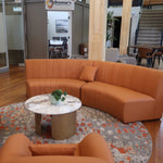 Orange sectional sofa in a modern office setting with a coffee table and plants.