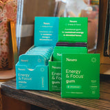 Neuro Energy & Focus mints and gum packaging on a wooden surface with a blurred background.