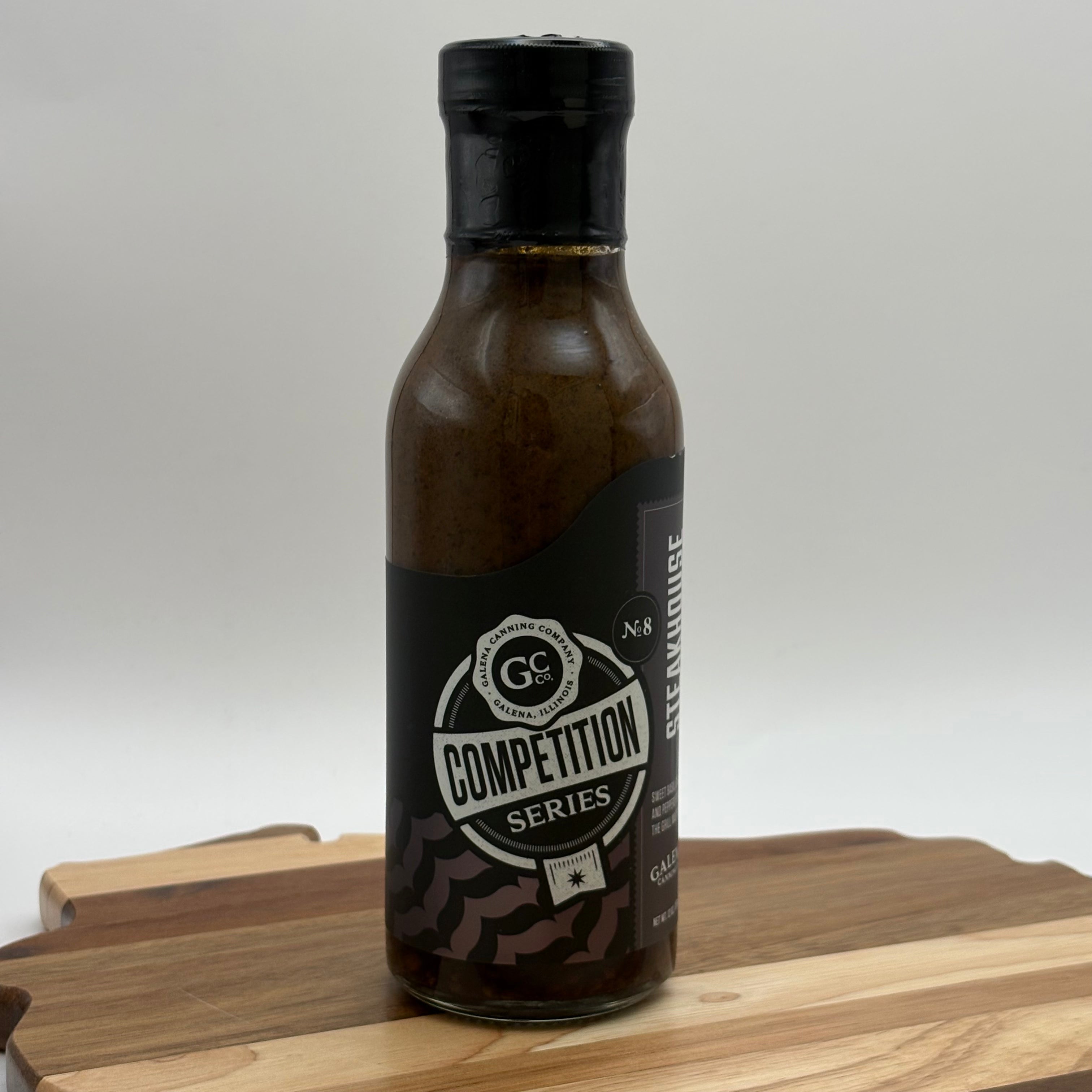 Bottle of Competition Series sauce on a wooden cutting board with a white background