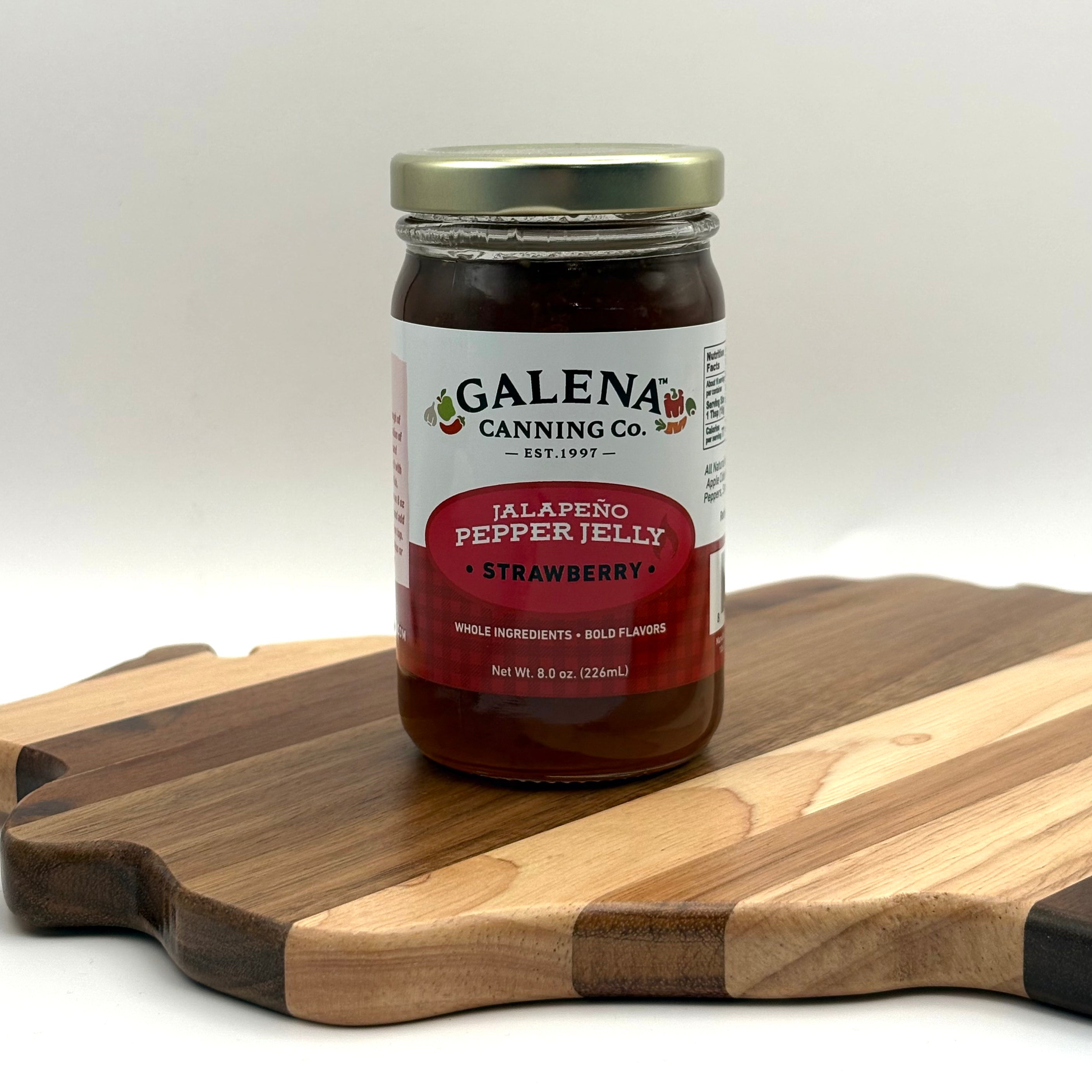Jar of Galena Canning Co. strawberry jalapeño pepper jelly on a wooden cutting board.