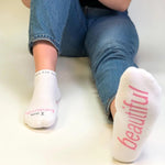 White socks with pink text worn by a person sitting on a white surface.