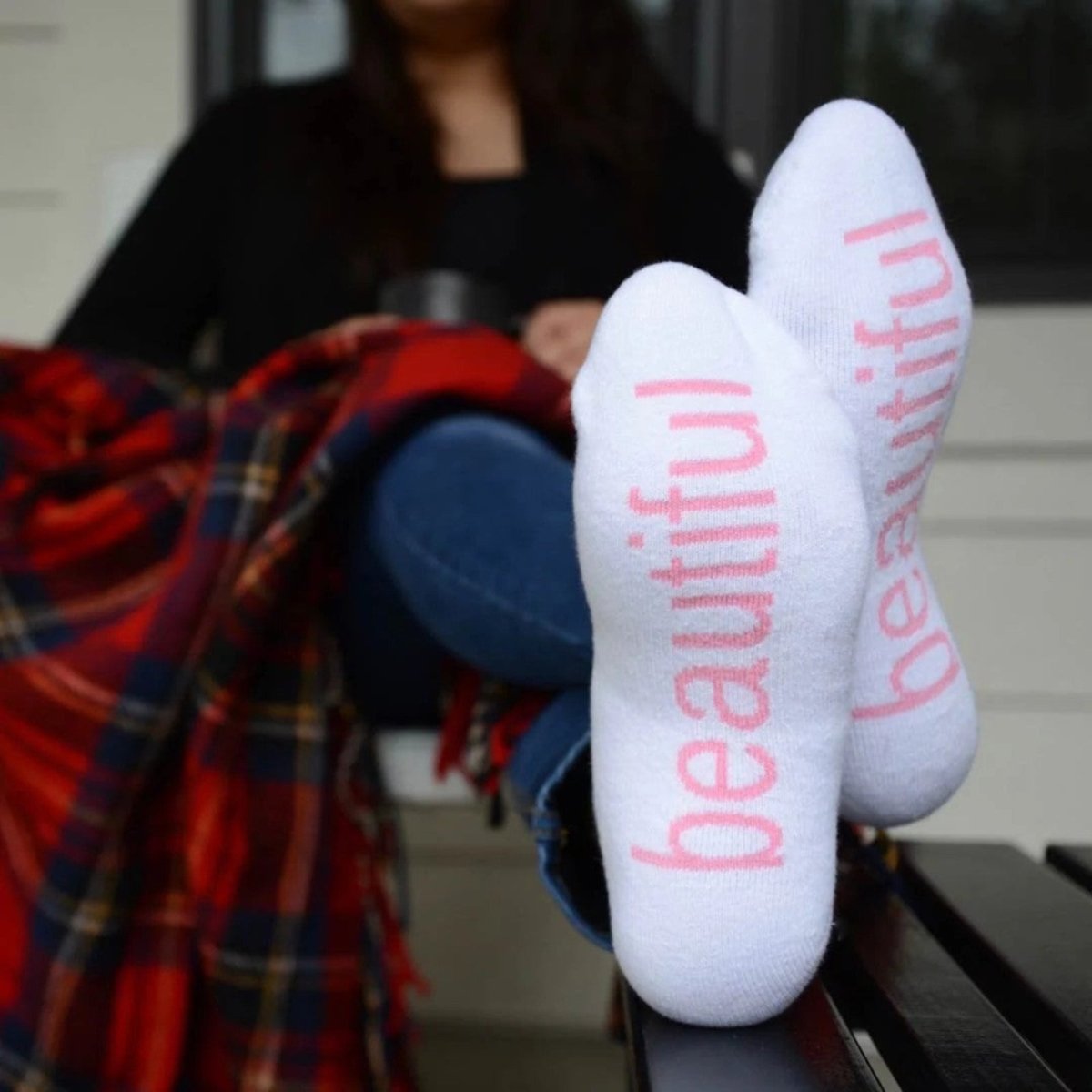 White socks with 'beautiful' printed in pink on a person sitting outdoors.