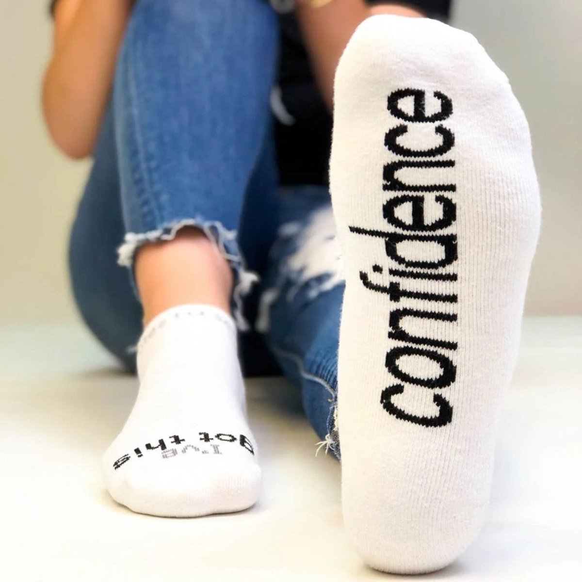 White socks with 'confidence' text worn by a person sitting on a white floor.