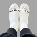 White socks with 'I've got this' text worn by a person on a gray background