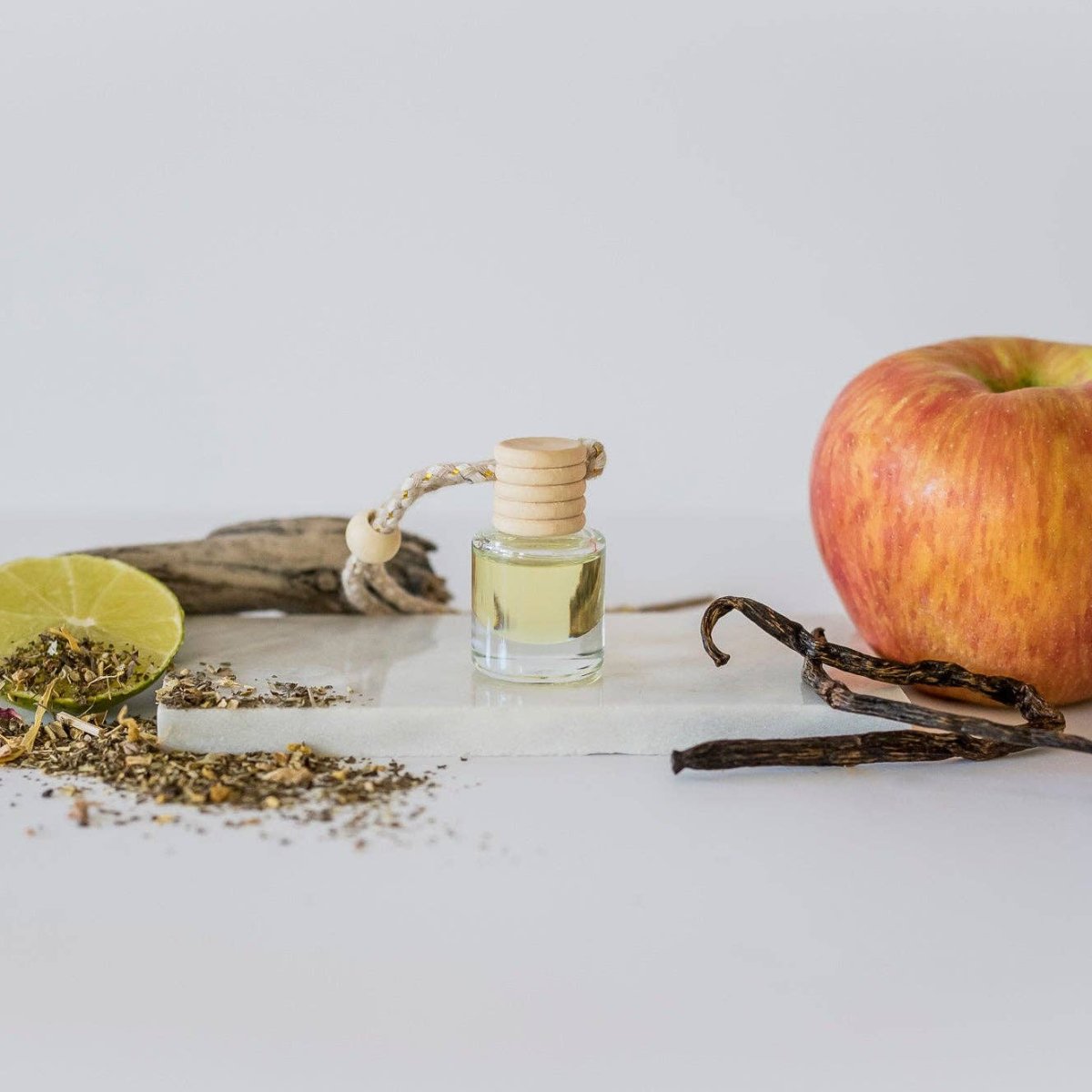 Small bottle of oil, apple, vanilla bean, and dried herbs on a white surface