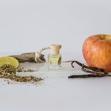 Small bottle of oil, apple, vanilla bean, and dried herbs on a white surface