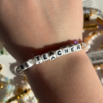 Little Words Project Bracelet with 'Number 1 Teacher' beads on a wrist against a blurred background