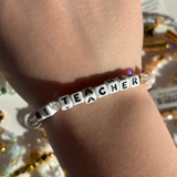 Little Words Project Bracelet with 'Number 1 Teacher' beads on a wrist against a blurred background