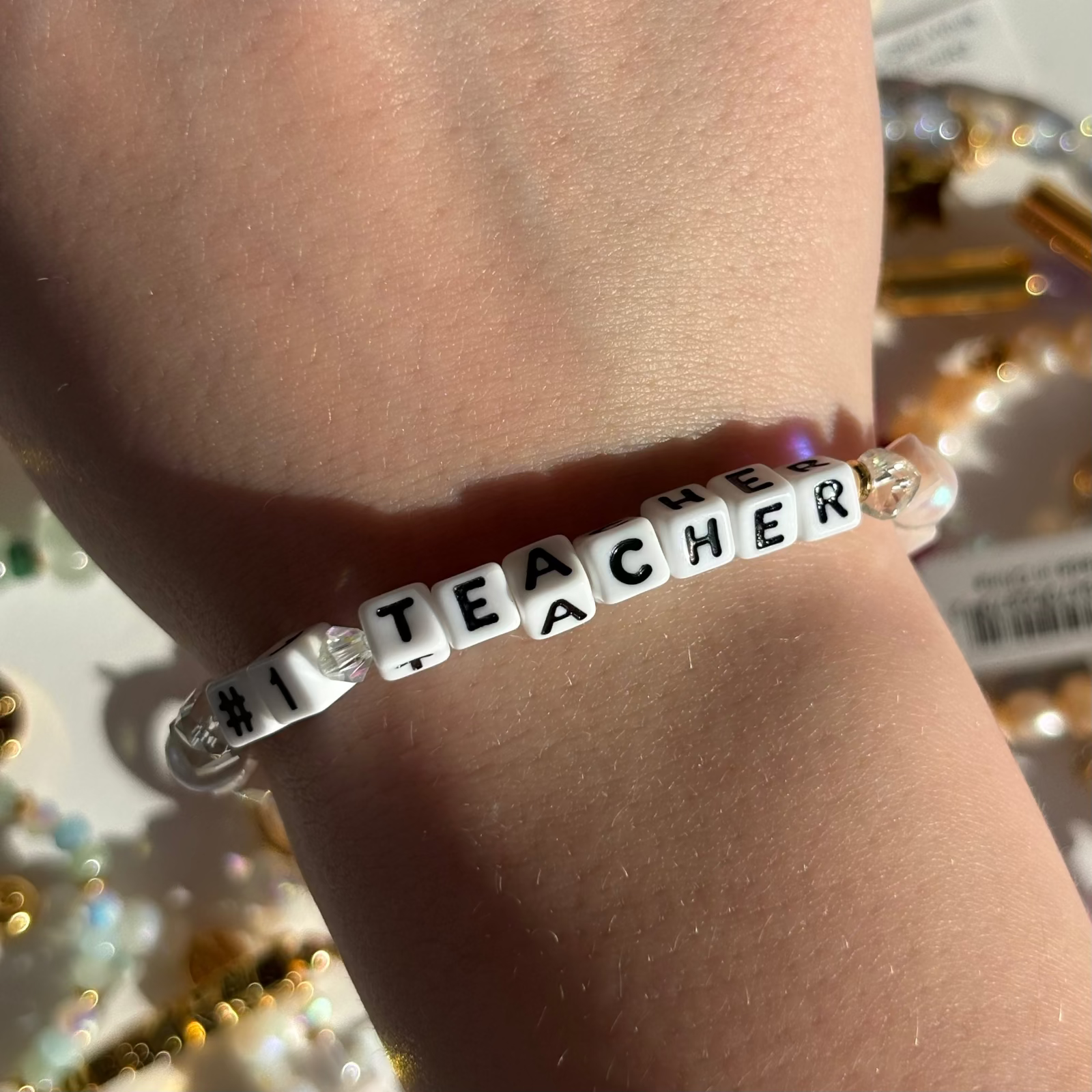 Little Words Project Bracelet with 'Number 1 Teacher' beads on a wrist against a blurred background