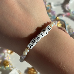 Little Words Project Bracelet with 'AUNTIE' beads on a wrist against a blurred background