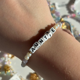 Little Words Project Bracelet with 'AUNTIE' beads on a wrist against a blurred background