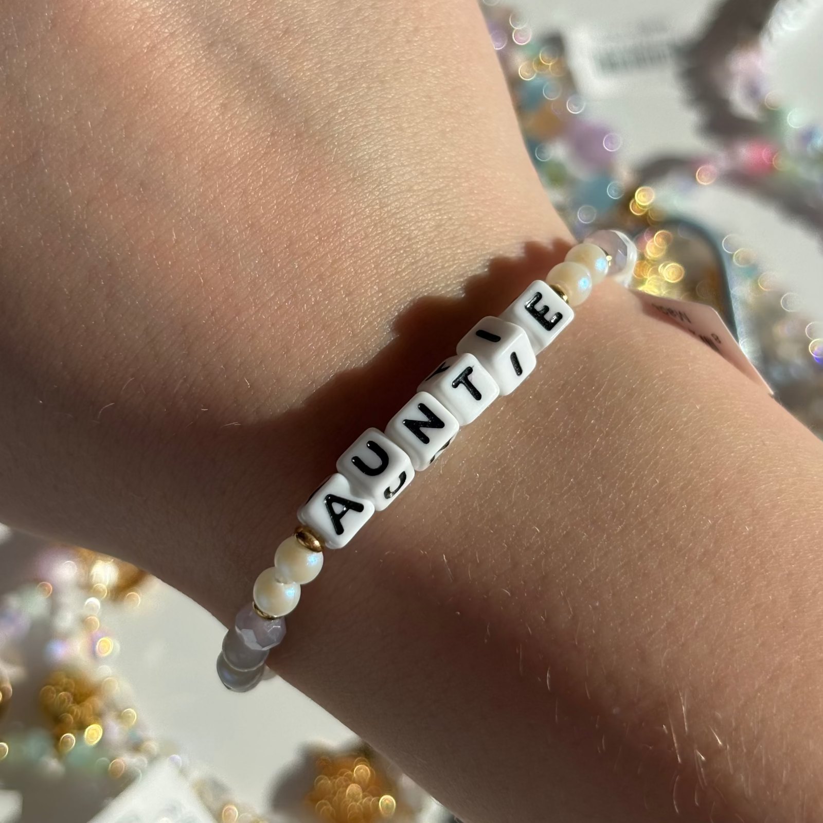 Little Words Project Bracelet with 'AUNTIE' beads on a wrist against a blurred background