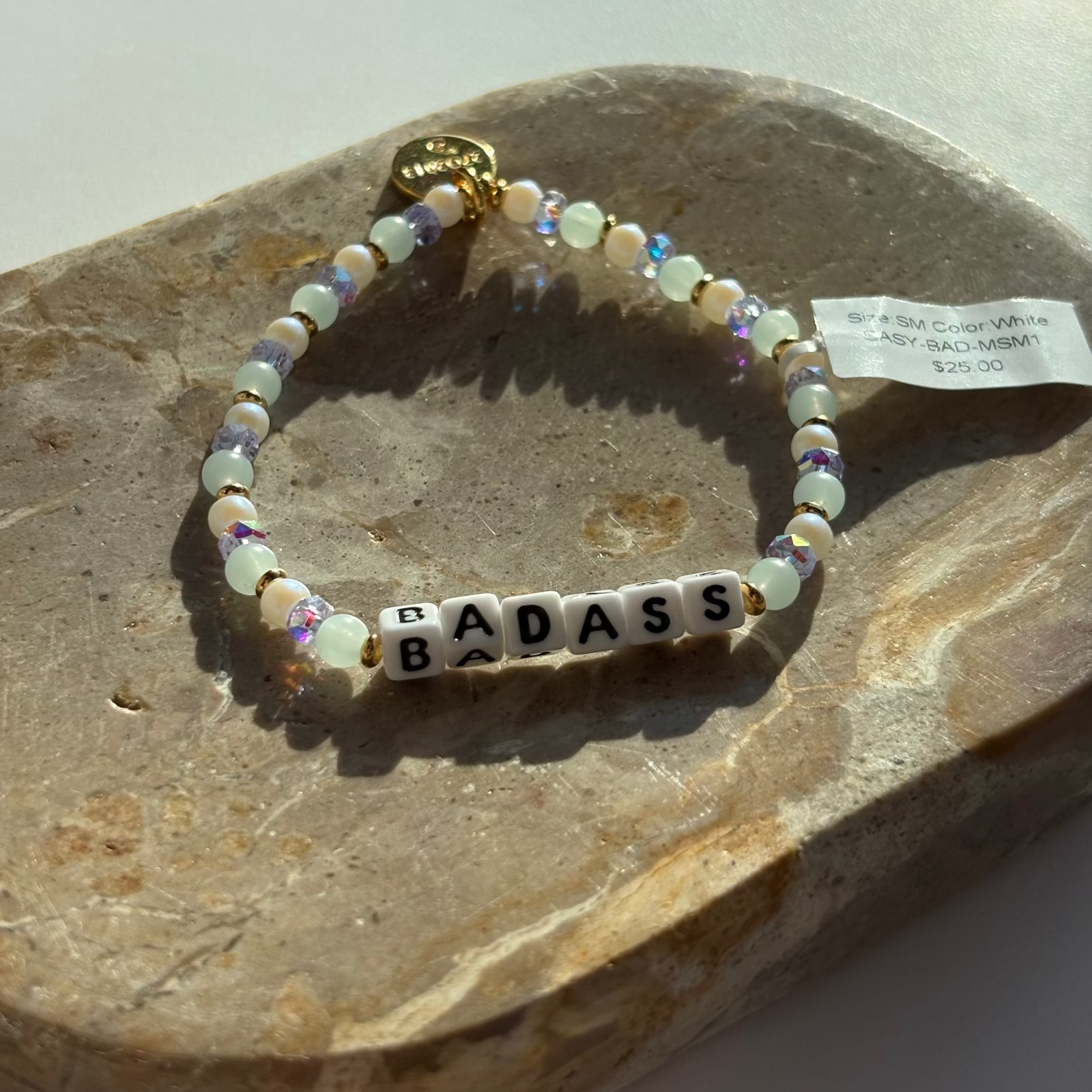 Little Words Project Bracelet with 'BADASS' beads on a stone surface