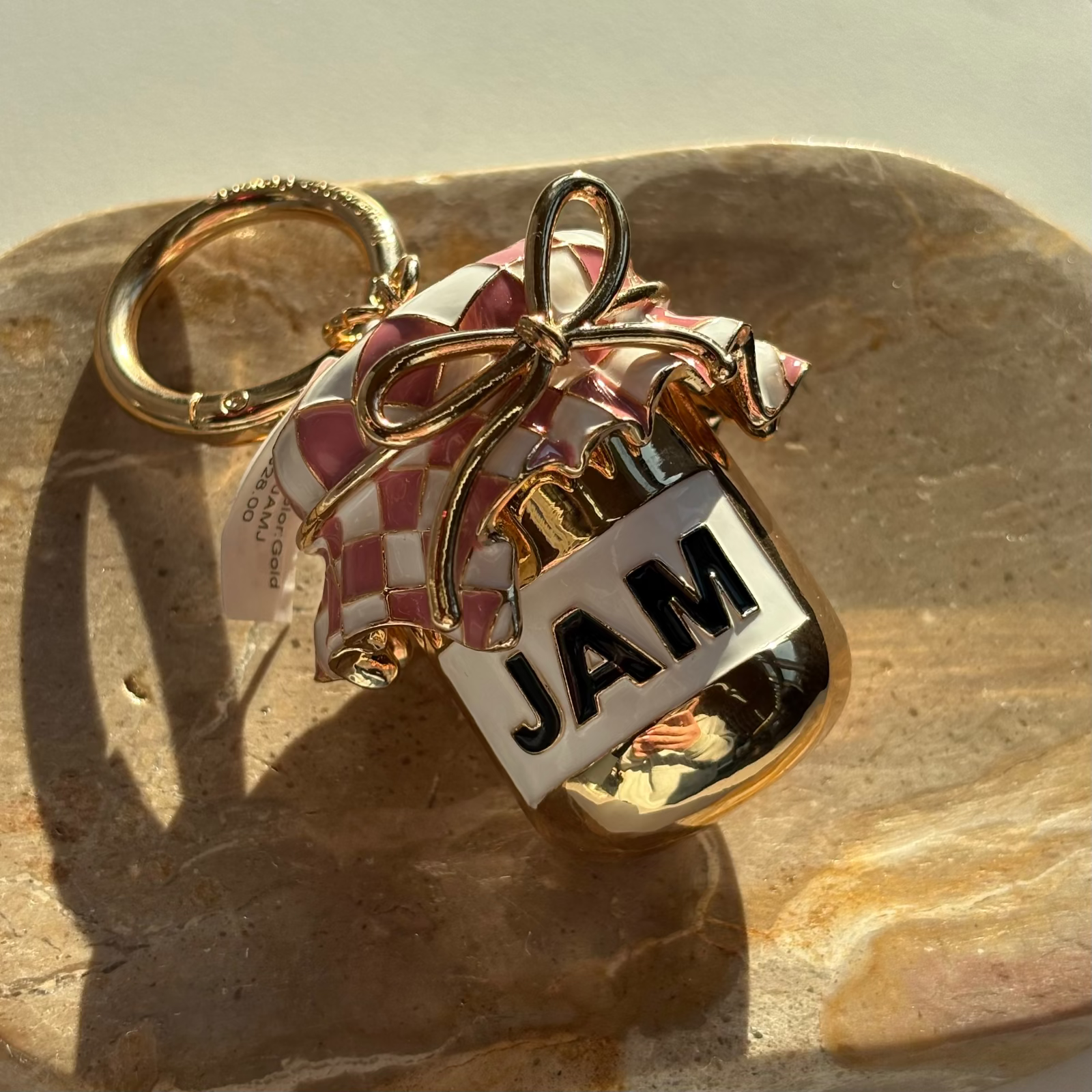 Little Words Project Keychain with checkered heart, gold bow, and 'JAM' tag on a stone surface
