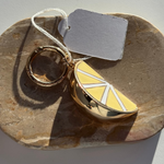 Gold ring and lemon-shaped bag charm on a stone surface with a tag.