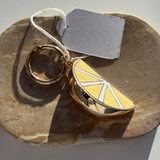 Gold ring and lemon-shaped bag charm on a stone surface with a tag.