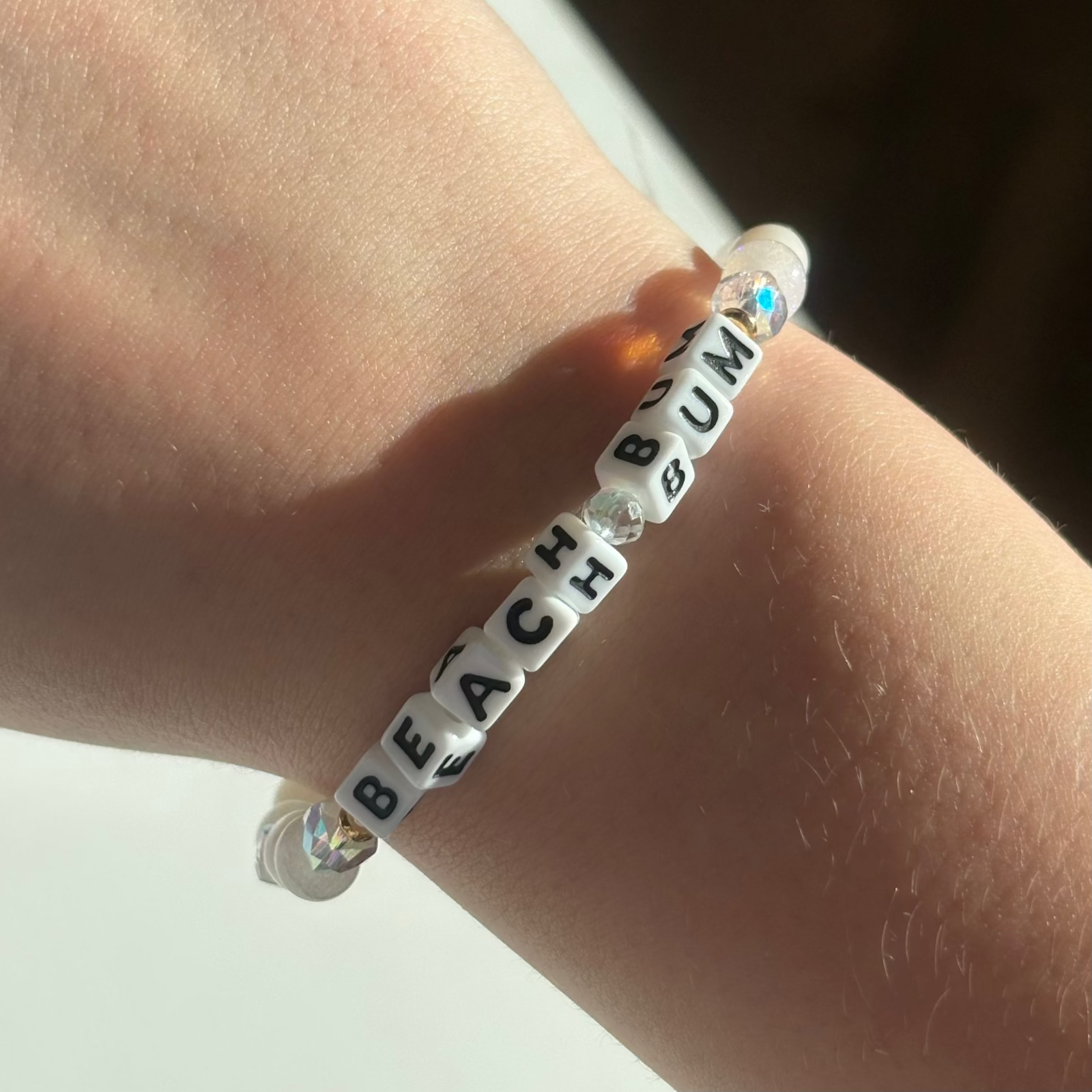Little Words Project Bracelet with 'BEACH BUM' beads on a wrist against a neutral background