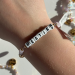 Little Words Project Bracelet with 'BESTIES' beads on a wrist, with jewelry in the background