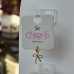 Gold bow charm on a 'Little Words Project Charms' card with a blurred background