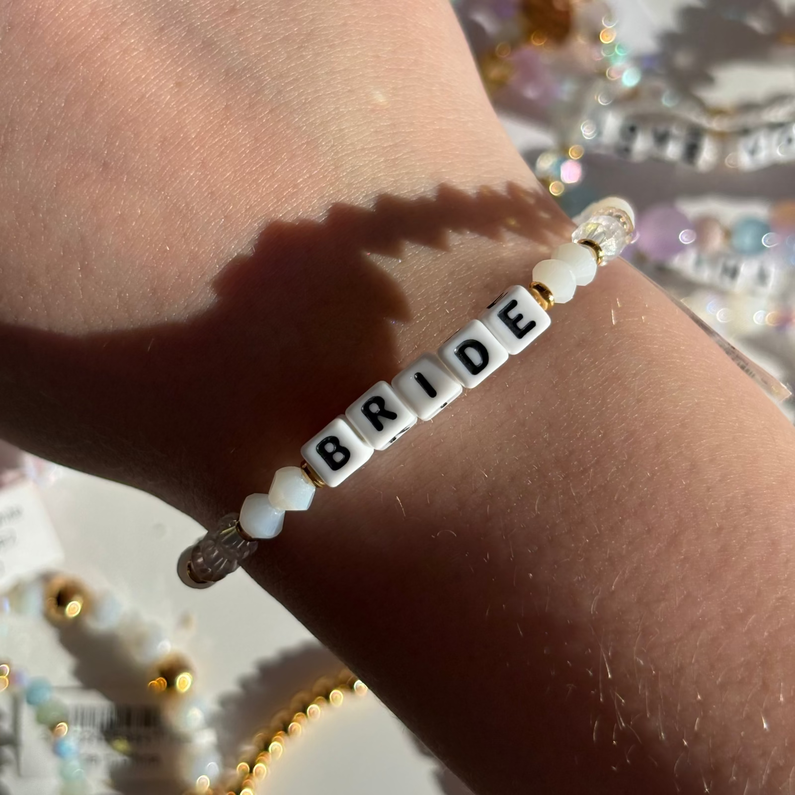 Little Words Project Bracelet with 'BRIDE' beads on a wrist against a blurred festive background