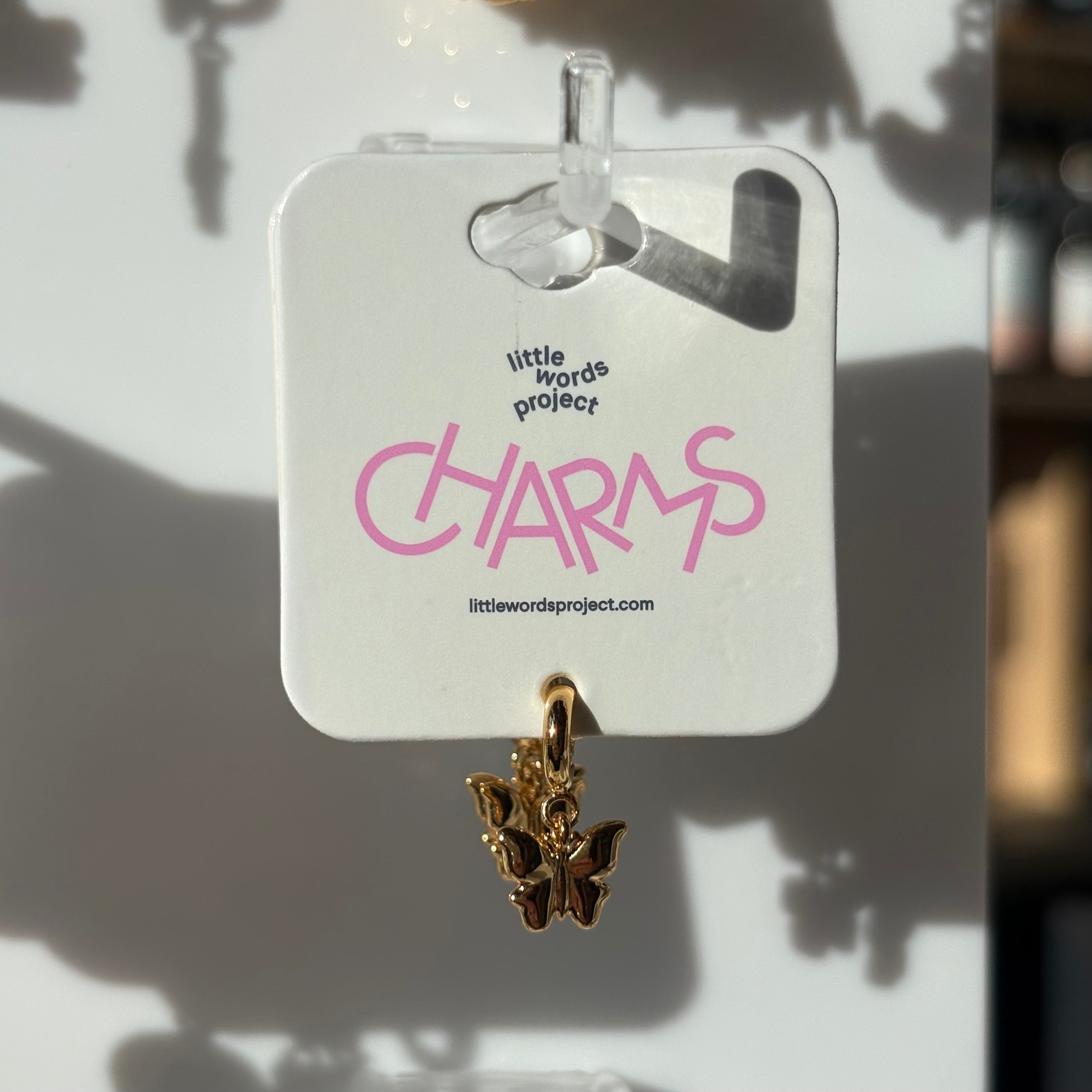 Gold butterfly charm on a 'Little Words Project' card with pink text.