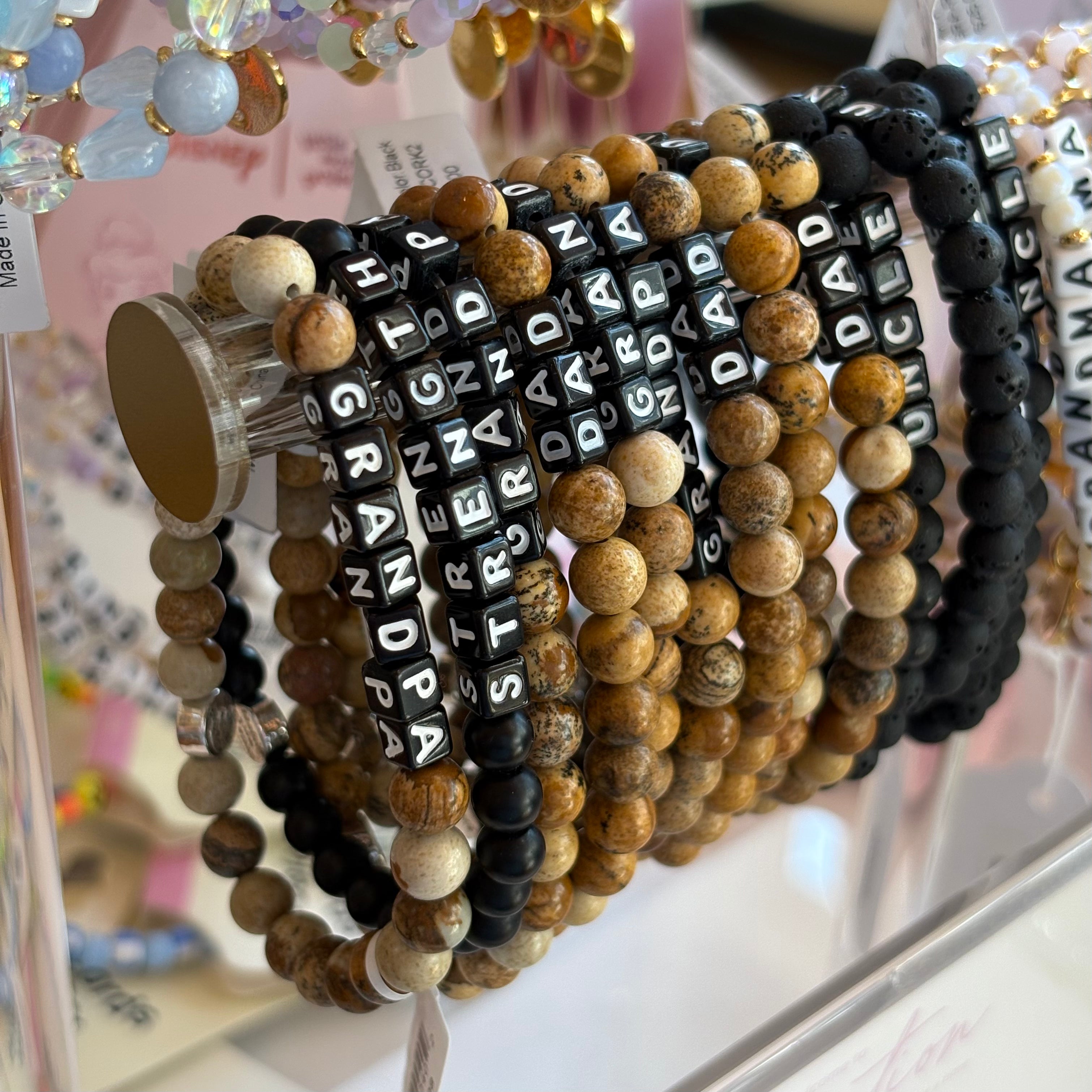Set of beaded bracelets with engraved text on a clear stand.