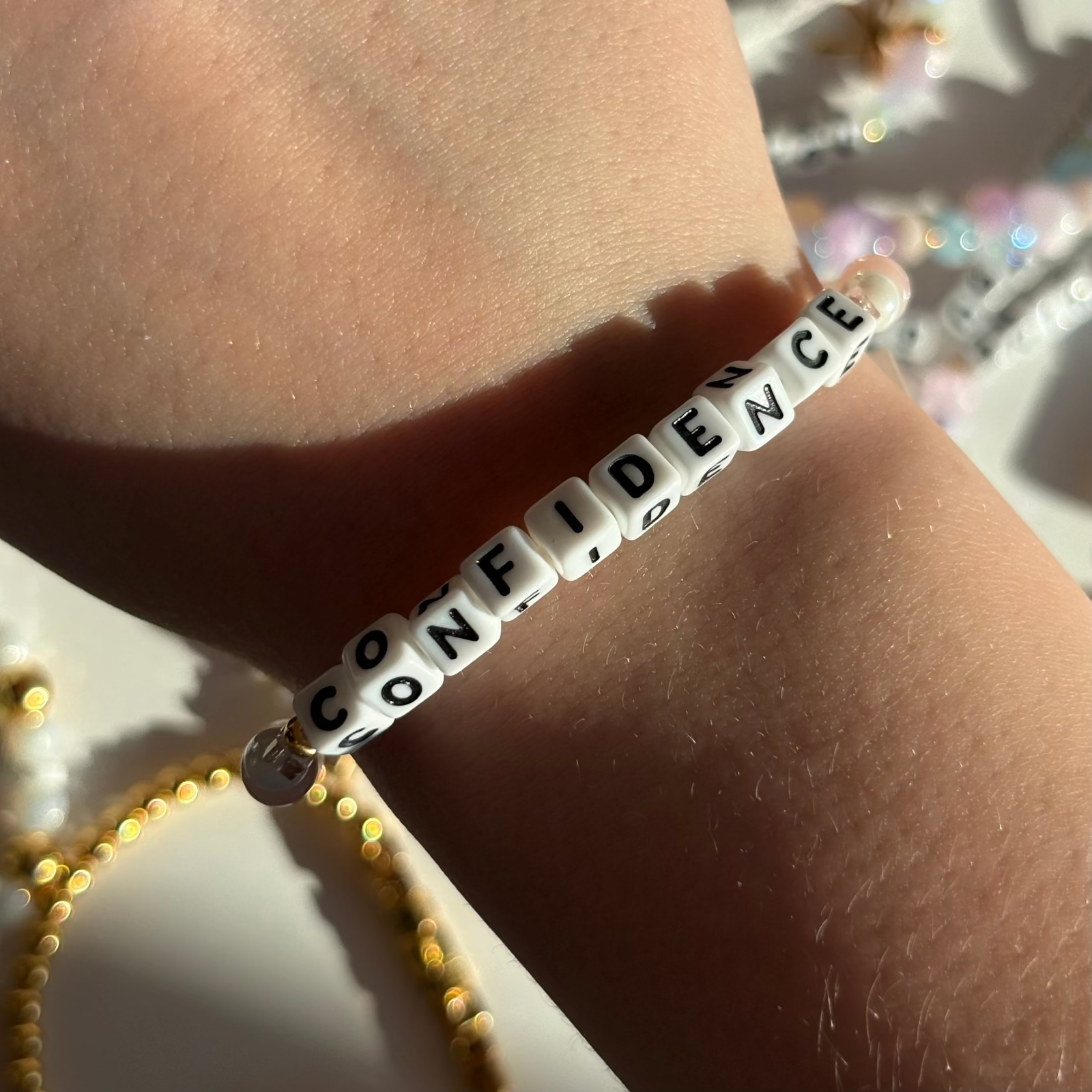 Little Words Project Bracelet with 'CONFIDENCE' beads on a wrist against a glittery background