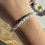 Little Words Project Bracelet with 'DAUGHTER' beads on a wrist against a marble background
