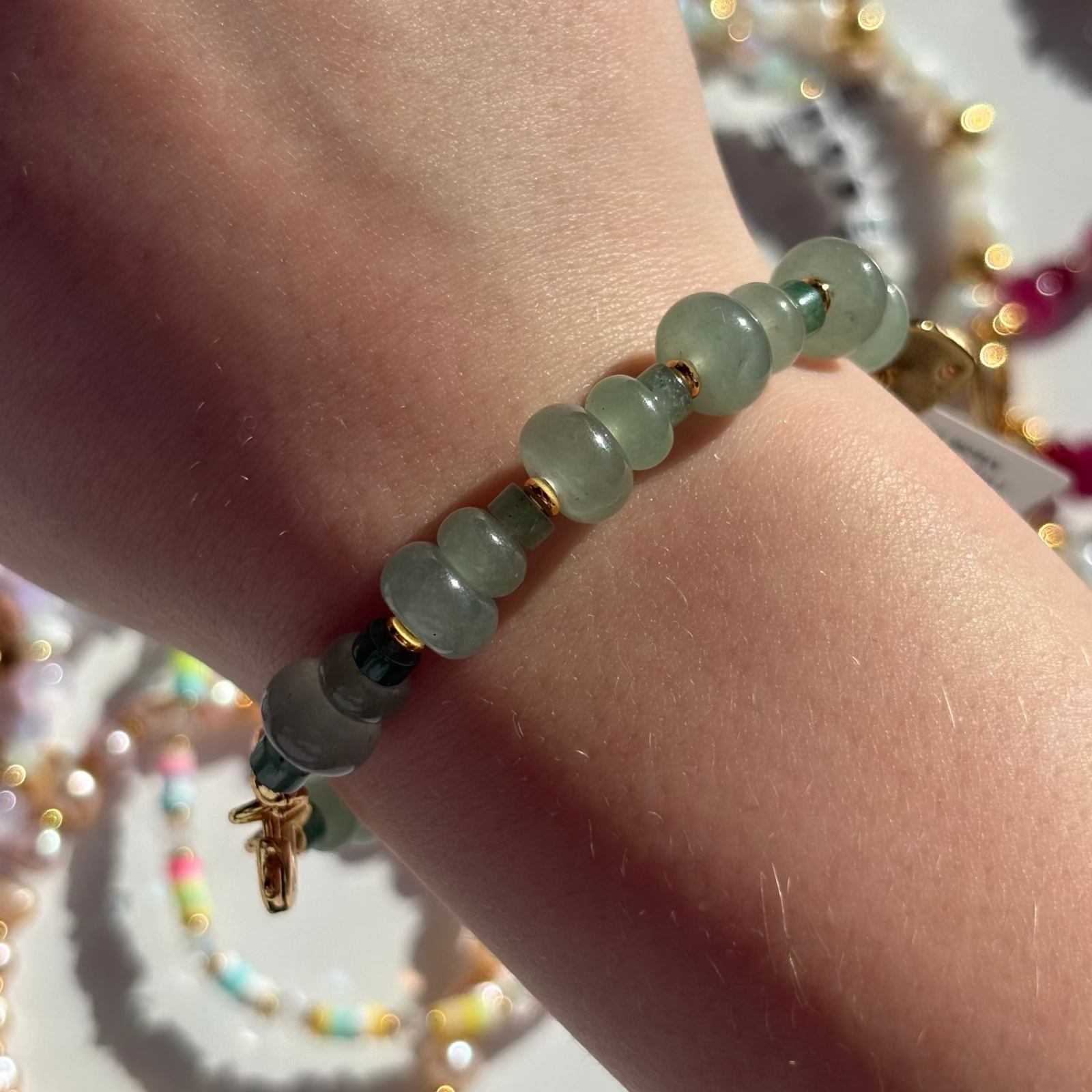 Little Words Project Dinner Party Green beaded bracelet on a wrist with blurred jewelry in the background
