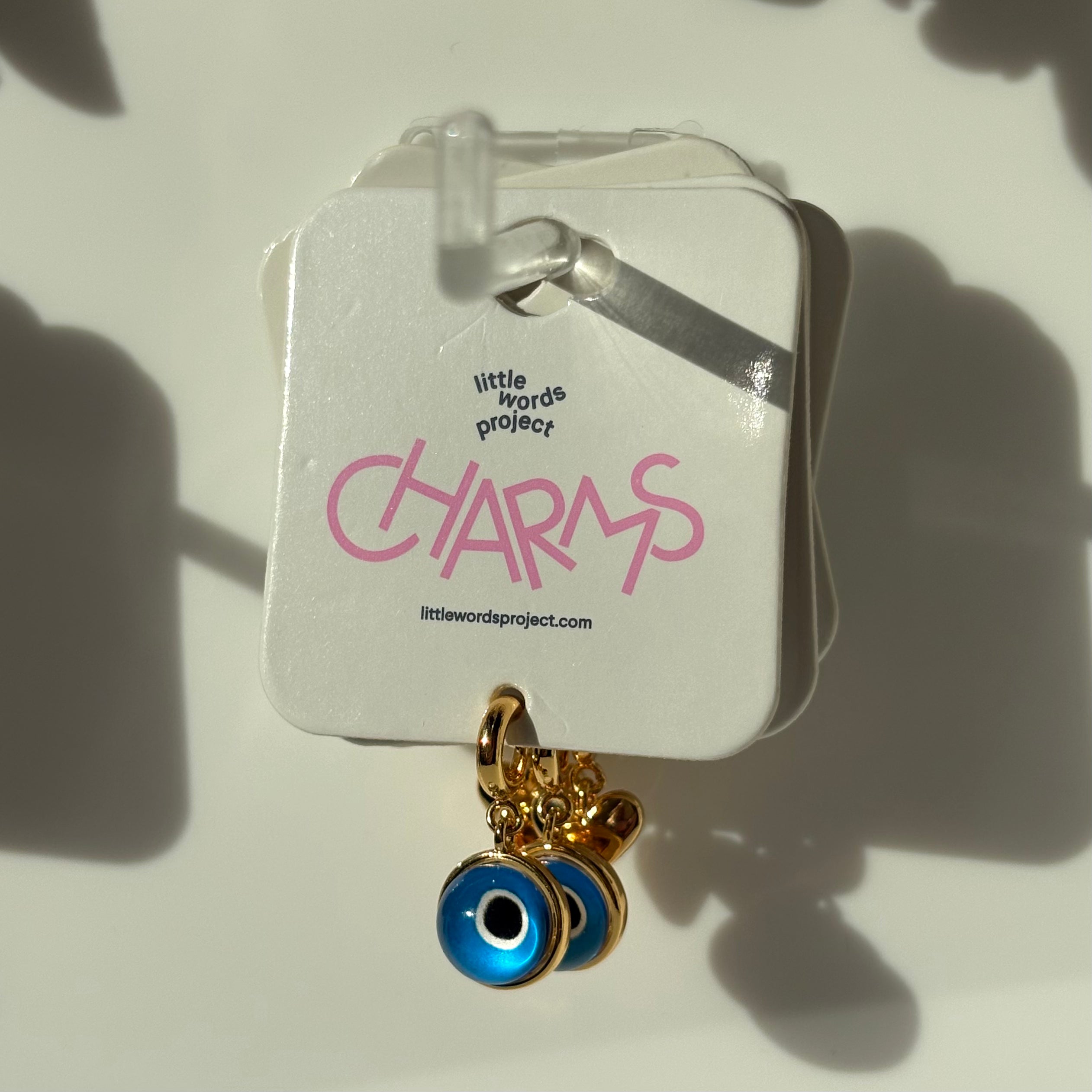 Evil eye charm on a 'little words project' card with pink text.